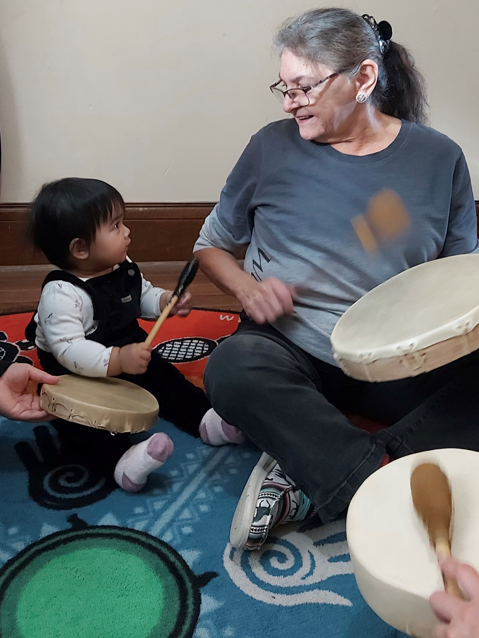 An elder shows an infant how to drum