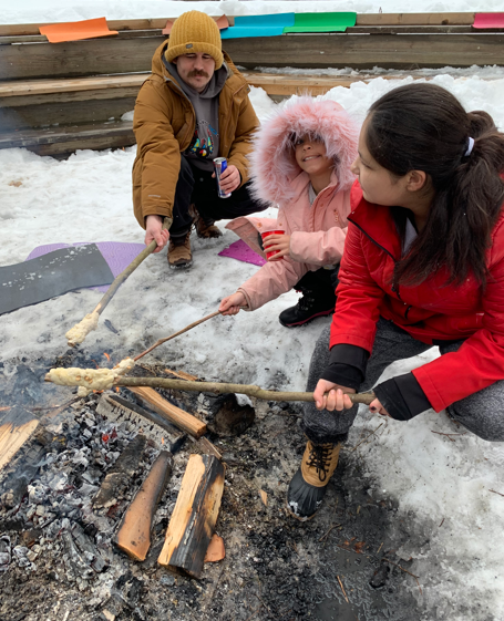 3 people cooking Bannock over a fire