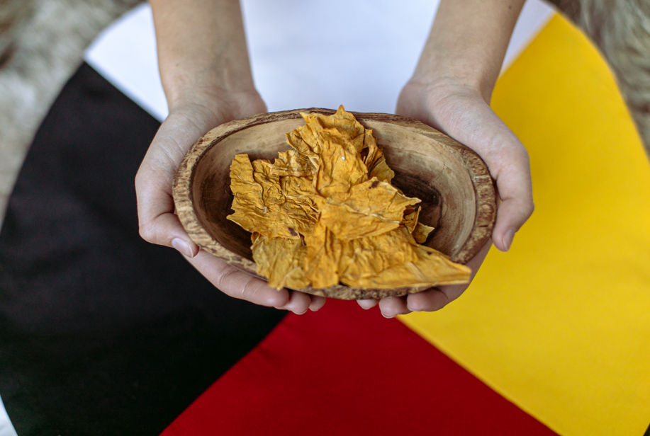 Natural tobacco in a wooden bowl being held. Medicine wheel in the background